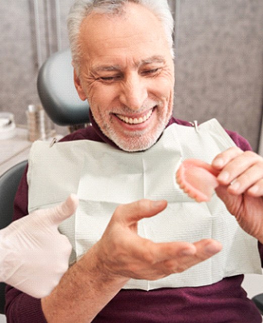 Smiling patient holding model of denture with dentist