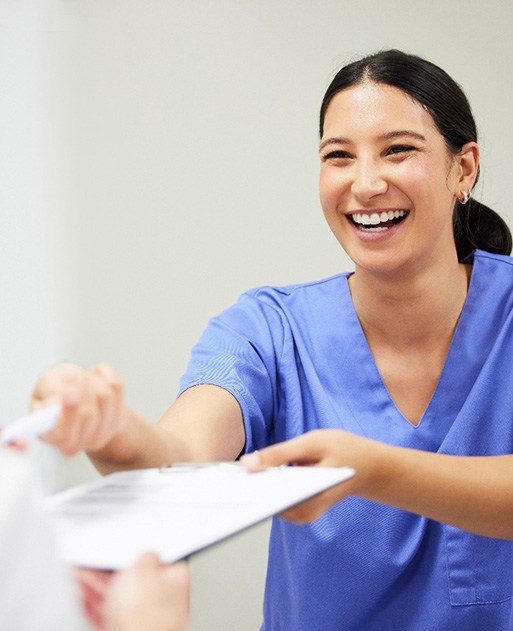 Dental assistant smiling while handing patient form