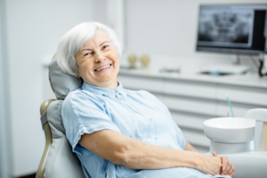 Woman with dentures smiling in dentist’s chair 